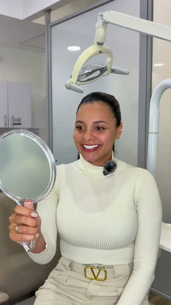 Paciente del Dr. Carlos Paz mirándose la sonrisa en un espejo, en su video testimonial